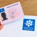 Carte de permis de conduire français tenue à la main, posée sur une enveloppe des Allocations familiales, illustrant les aides disponibles pour financer le permis.