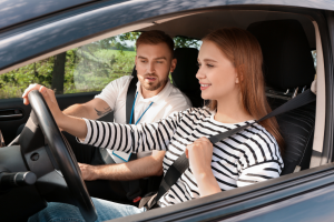 Jeune femme souriante apprenant à conduire avec un moniteur d’auto-école à ses côtés dans une voiture, tous deux attachés et concentrés.