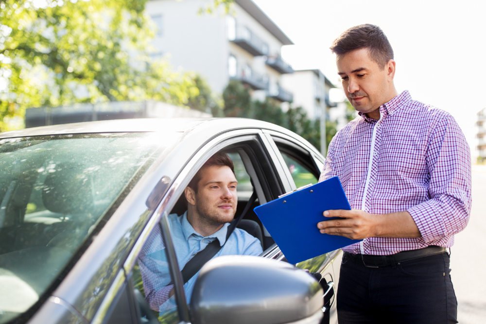 Élève et formateur en discussion dans une voiture, carnet d’évaluation à la main.