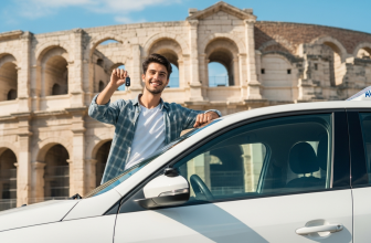 Jeune conducteur souriant tenant ses clés devant une voiture auto-école avec les Arènes d'Arles en arrière-plan